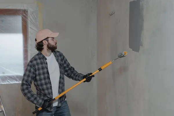 Painter rolling grey paint onto an interior wall in Oxnard